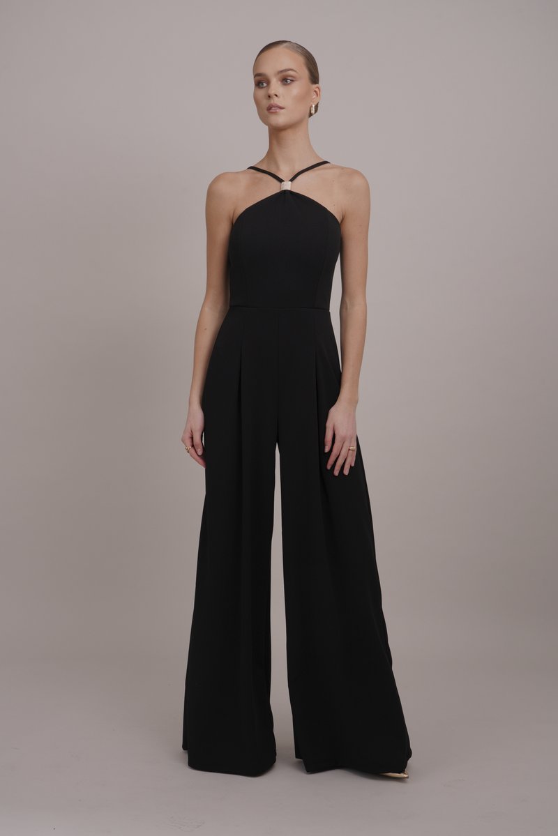 Giubbotto nero con corpino aderente, scollo all'americana e pantaloni a gamba larga. Presenta pince in vita e un accentuato hardware decorativo.