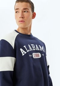 Marineblaue Sweatshirt mit Raglanärmeln in Creme, mit dem Aufdruck "ALABAMA" und einer Jahressgrafik. Weicher Stoff.