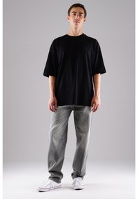 Schwarzes, übergroßes T-Shirt, kurze Ärmel, entspannter Schnitt. Getragen mit ausgewaschenen, hellgrauen Jeans und weißen Sneakers mit niedrigem Schnitt. Einfaches Design, keine sichtbaren Muster.