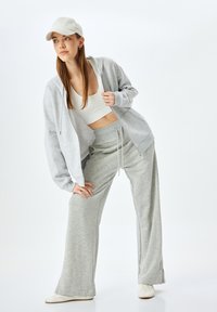 Felpa grigia chiaro con zip, pantaloni sweatpants a gamba larga coordinati e un crop top bianco. Il tessuto è morbido, con un taglio rilassato e dettagli minimi.