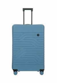 Valigia rigida di colore azzurro chiaro, con design a texture ondulata, maniglia telescopica e quattro ruote girevoli nere per una maggiore manovrabilità.