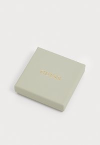 Vierkante lichtgroene cadeau doos met een gestructureerde afwerking en een gouden reliëf "GUESS" logo op de bovenkant.