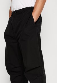 Schwarze, locker sitzende Hosen aus leichtem Stoff, mit elastischem Bund, Seitentaschen und minimalen Details.