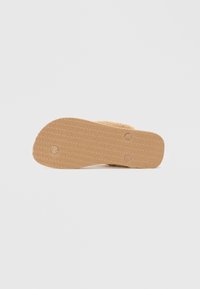 Tan gummisåle med teksturert overflate og to sirkulære innkapp. Mykt, fluffy materiale festet til den øvre delen. Minimalistisk design.