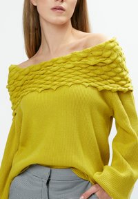 Maglione giallo a spalle scoperte con motivo testurizzato e in rilievo all'altezza del collo, corpo a coste e maniche larghe, abbinato a pantaloni a quadrati.