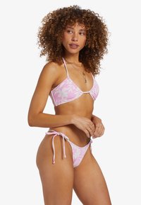 Completo bikini floreale rosa con top triangolare e slip con lacci laterali. Il tessuto ha una texture a coste con una finitura lucida.