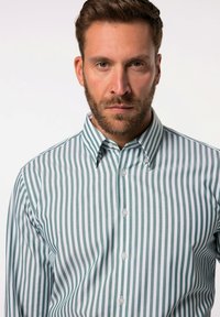 Camisa a rayas verdes y blancas con cuello abotonado, fabricada con un tejido texturizado y seis botones en la parte delantera.