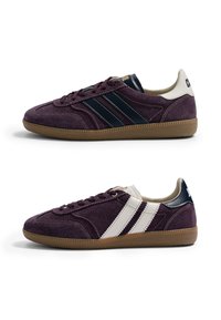 Paquet de baskets en daim violet foncé avec semelles en gomme, une affichant des bandes latérales noires, l'autre des bandes latérales blanches, toutes deux avec des languettes de talon contrastantes.
