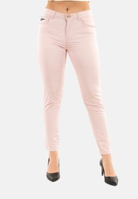 Pantalones ajustados de color rosa claro con textura suave, cierre de botón y bolsillos frontales, combinados con tacones altos negros.