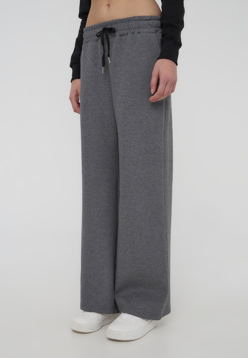Pantaloni della tuta grigi a gamba larga con vita elastica e cordino. Il tessuto sembra morbido e comodo, con una consistenza liscia.