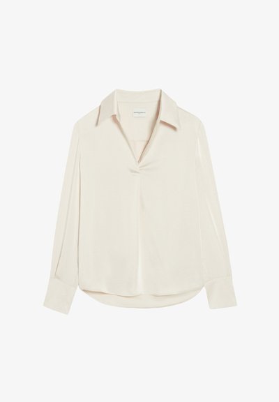 Blusa beige chiaro realizzata in tessuto morbido, con colletto a punta, maniche lunghe e una discreta patta frontale.