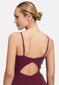 Robe bordeaux avec de fines bretelles, détail de dos découpé et un tissu texturé, scintillant. Conçue avec une silhouette ajustée.