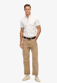 Wit T-shirt met korte mouwen, met knoopdetails en een borstzak, gecombineerd met lichtbeige broeken en beige sneakers. Gladde stoftextuur.