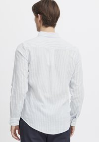 Camisa de mangas largas a rayas en azul claro y blanco, con un dobladillo redondeado y puños abotonados. Fabricada con una tela suave y texturizada.