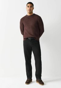 Burgundi kötött pulóver kerek nyakkal, fekete nadrág és barna velúr cipő. A modell a hátul tartott kezével áll, semleges háttér előtt.