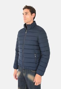 Giacca imbottita blu marino con colletto alto, chiusura con zip e due tasche laterali. Presenta cuciture orizzontali e una trama liscia.