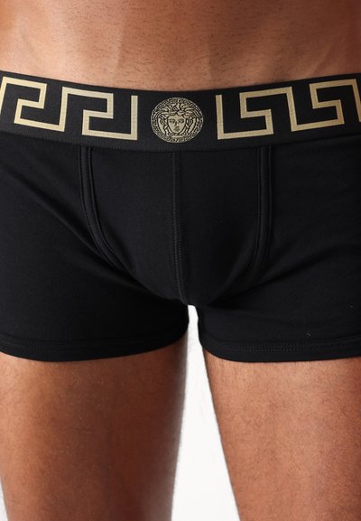 Black cotton boxer shorts with a gold-accented waistband featuring a Greek key pattern and a central Medusa logo. Smooth texture.