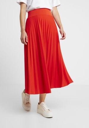 Pleated mid-length skirt in bright red, featuring a wide waistband. Paired with light-colored sneakers, against a plain white background.