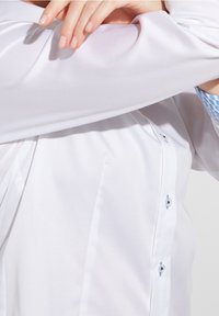 Chemise blanche à manches longues avec une texture lisse ; présente des accents bleus aux poignets et aux boutons, mettant en avant un design classique.