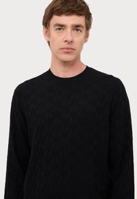Maglione nero a maglia con un motivo testurizzato su tutta la superficie, colletto rotondo e maniche lunghe, caratterizzato da una leggera lucentezza e un tessuto morbido.