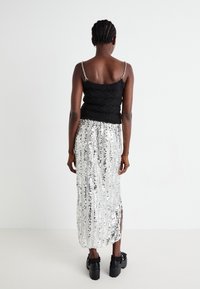 Top en tricot noir avec une jupe maxi en sequins argentés dotée de rayures verticales, d'une fente sur le côté et de chaussures à talons épais noires avec des accents froncés.