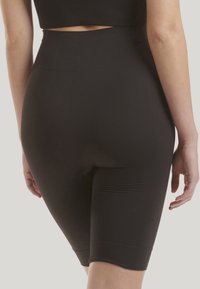 Černé žebrované šortky s vysokým pasem a hladkou texturou, které mají délku do poloviny stehna a bezšvový design. Obsahují výřezový detail.