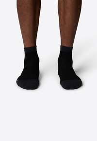Svarta ankelsockor med ribbad manchet och förstärkta häl- och tåkonstruktioner, slät textur och minimal märkning på sidan.