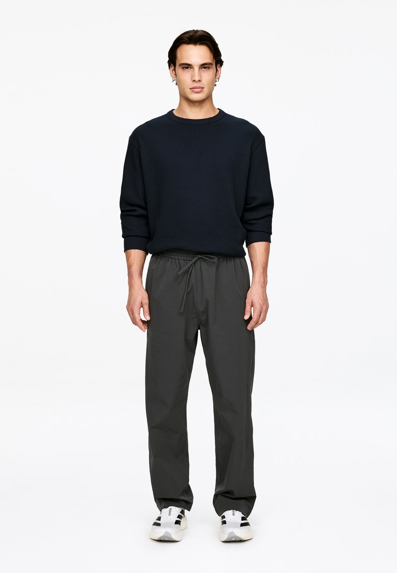 Pull texturé bleu foncé avec un col rond, accompagné d'un pantalon gris ample et de chaussures de sport noir et blanc.