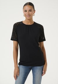 Melns T-kreklis ar mež ģīņu piedurknēm, apaļu kakla izgriezumu, brīvu piegriezumu un mīkstu audumu. Piedurknes ir ar ziedu mežģīņu rakstu, kas piešķir papildus detalizāciju.