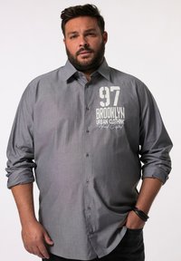 Camicia grigia con bottoni e maniche lunghe, caratterizzata da una stampa grafica bianca con la scritta "97 BROOKLYN URBAN CLOTHING". Texture liscia, vestibilità classica.