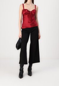 Top de satén rojo con un escote fruncido y detalle de ojal, combinado con pantalones de pierna ancha negros y botas de tobillo puntiagudas negras.
