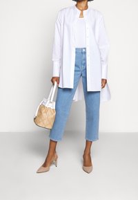 Valkoinen nappikauluspaita, jossa on pyöreä kaulus, vaaleansiniset lyhyet farkut, beige korkeat kengät ja vaaleanruskea ämpärilaukku, jossa on valkoisia yksityiskohtia.