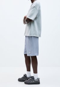 Chemise courte à manches courtes oversize gris clair, shorts côtelés bleus et baskets de sport noires avec des accents gris et des chaussettes blanches.