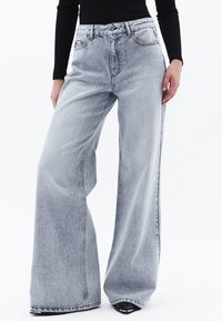 Jeans de mezclilla gris claro de pierna ancha con una alta cintura, que cuentan con un cierre de botón, bolsillos laterales y detalles de costura visibles.