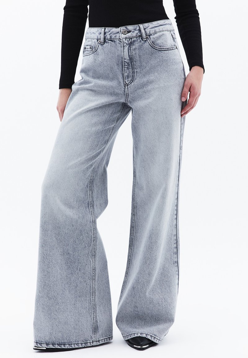 Jeans de mezclilla gris claro de pierna ancha con una alta cintura, que cuentan con un cierre de botón, bolsillos laterales y detalles de costura visibles.