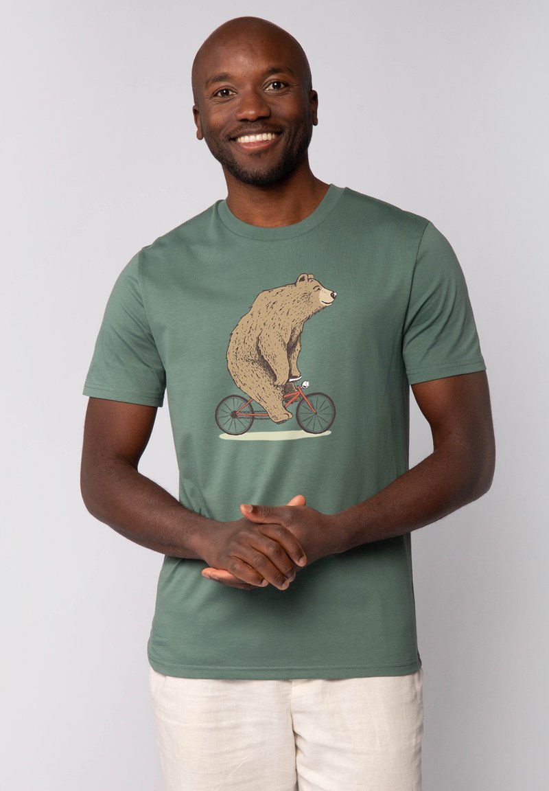Groen katoen t-shirt met een afbeelding van een beer die op een rode fiets rijdt. Korte mouwen, ronde halslijn, gladde textuur.