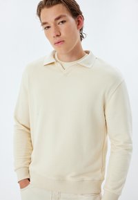 Beige pullover sweatshirt met V-hals en kraag, ribbels bij de mouwen en onderrand. Soepele textuur met een ontspannen pasvorm.