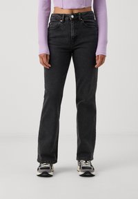 Black denim jeans with a straight leg fit, five-pocket design, and contrasting stitching, paired with a light purple top and athletic shoes.