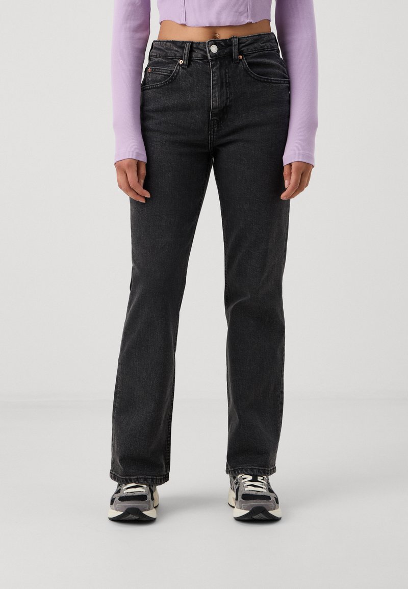 Black denim jeans with a straight leg fit, five-pocket design, and contrasting stitching, paired with a light purple top and athletic shoes.