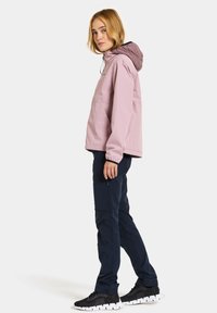 Ljusrosa vattentät jacka med dragsko i huvan, i kombination med marinblå byxor. Outfitten har en avslappnad passform och funktionella fickor.