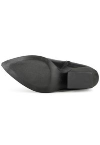 Zapato negro con punta afilada, suela de goma texturizada y plana, y tacón bajo en bloque. El diseño superior presenta un acabado liso y costuras sutiles.