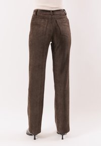 Pantaloni marroni con trama, design a gamba dritta; dotati di due tasche posteriori e cintura con passanti.