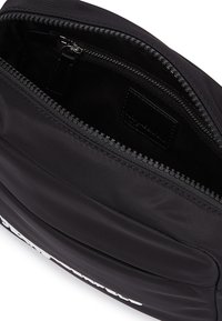 Geantă crossbody din nylon negru, cu o textură netedă, design curbat, închidere cu fermoar în partea de sus și un buzunar interior cu fermoar pentru organizație.