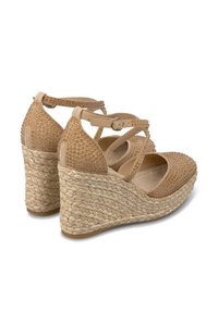 Sandalias de cuña beige con un tacón de yute trenzado, parte superior texturizada con pequeños remaches y correas de tobillo ajustables en cruz.