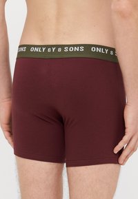 Bordowe bawełniane bokserki o jednolitym wzorze, z oliwkowozielonym elastycznym paskiem w talii z białym napisem "ONLY & SONS." Gładka faktura.