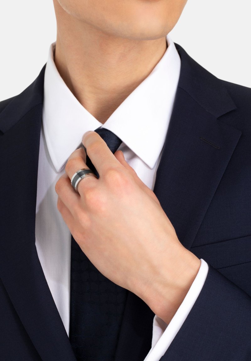 Marindräkt med en vit skjorta, som justerar en slips. Handen, som bär en silverring, är placerad vid halsen.