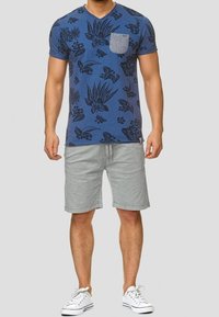 Short-sleeve blue T-shirt with dark floral prints and a gray pocket, paired with light gray shorts and white sneakers.