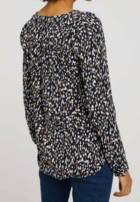 Blouse à manches longues bleu marine avec un motif tacheté en nuances de blanc et de beige, coupe décontractée et tissu doux et texturé.