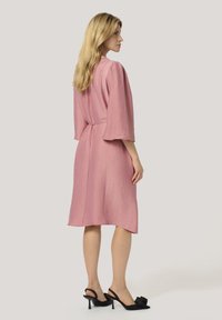 Rosa klänning med trekvartsärmar, bältesmidja och en strukturerad tyg, i kombination med svarta slingback-hälar med en blommig detalj.