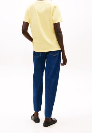Jasnożółta bawełniana koszulka z krótkim rękawem, w połączeniu z ciemnoniebieskimi dżinsami. Prosty fason, luźny krój i płaskie czarne buty.